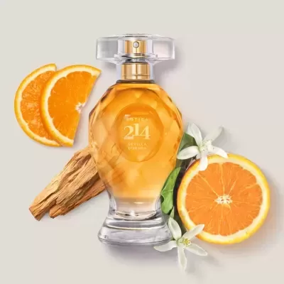 Frasco de perfume âmbar com tampa transparente e dourada, rodeado de rodelas de laranja e flores