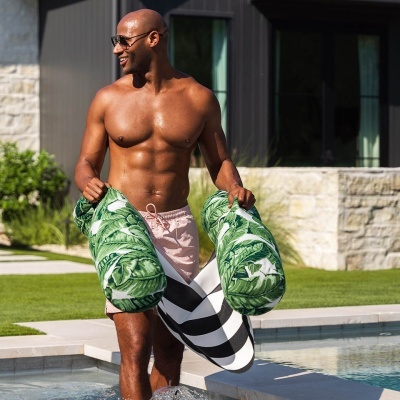 Homem com calção rosa e arm floaties verdes ao lado da piscina