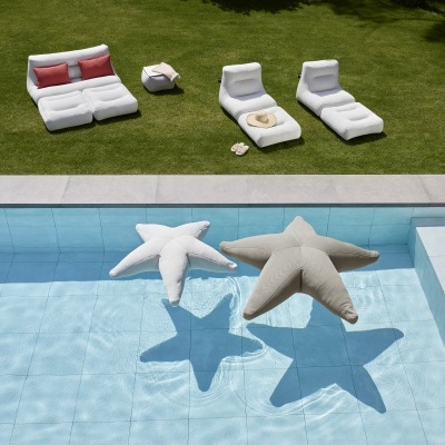 Mobiliário branco e cinza exterior com almofadas flotantes em forma de estrela numa piscina azul e relvado verde ao fundo