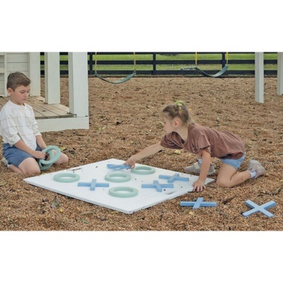 Jogo gigante xadrez com peças madeira azul e verde em painel branco no chão exterior, crianças a jogar.