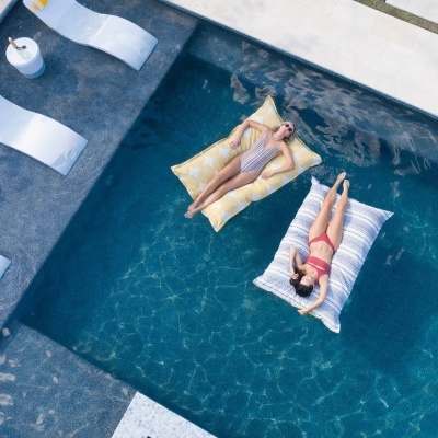Duas mulheres em colchões insufláveis com padrões amarelo e branco e azul e branco na piscina