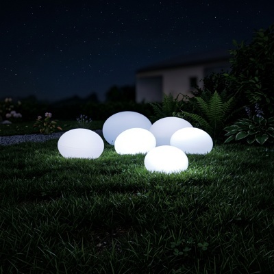 Lâmpadas esféricas brancas iluminadas no relvado à noite com plantas e casa ao fundo