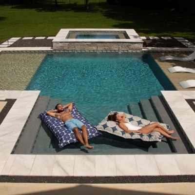 Piscina com borda em pedra branca e duas espreguiçadeiras flutuantes almofadadas com padrão azul e branca e de círculos cinzentos.