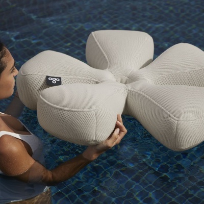 Almofada flutuante bege em forma de flor na piscina com mulher a segurá-la