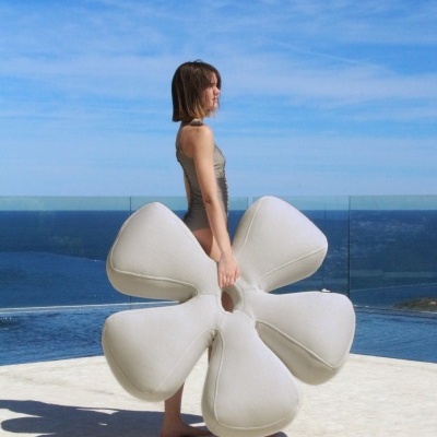 Mulher com fato de banho segurando almofada grande em forma de flor no terraço com vista para o mar.