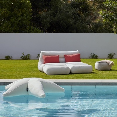 Mobiliário exterior bege claro com almofadas vermelhas ao lado de piscina