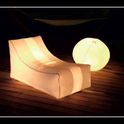 Cadeira lounge inflável iluminada e esfera luminosa branca sobre pavimento em madeira.