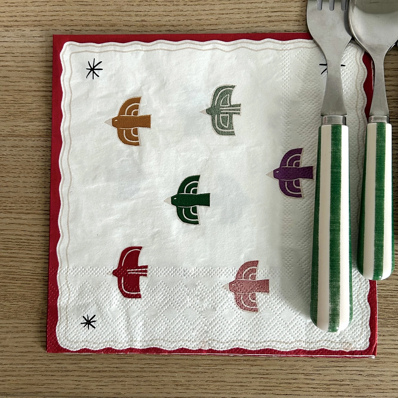 Guardanapo branco com padrão de pássaros coloridos e talheres com cabo riscado verde e branco