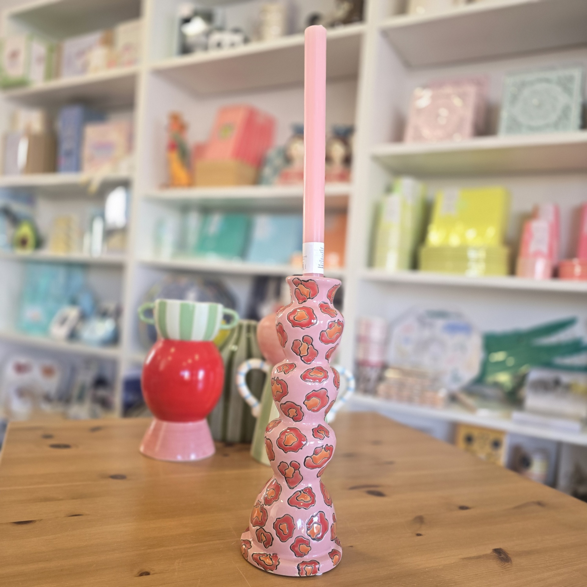 Castiçal de cerâmica rosa com padrão animal print e vela rosa sobre mesa de madeira