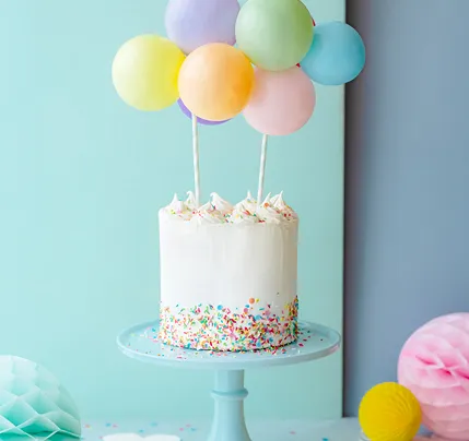 Bolo branco decorado com granulados coloridos e balões coloridos suspensos