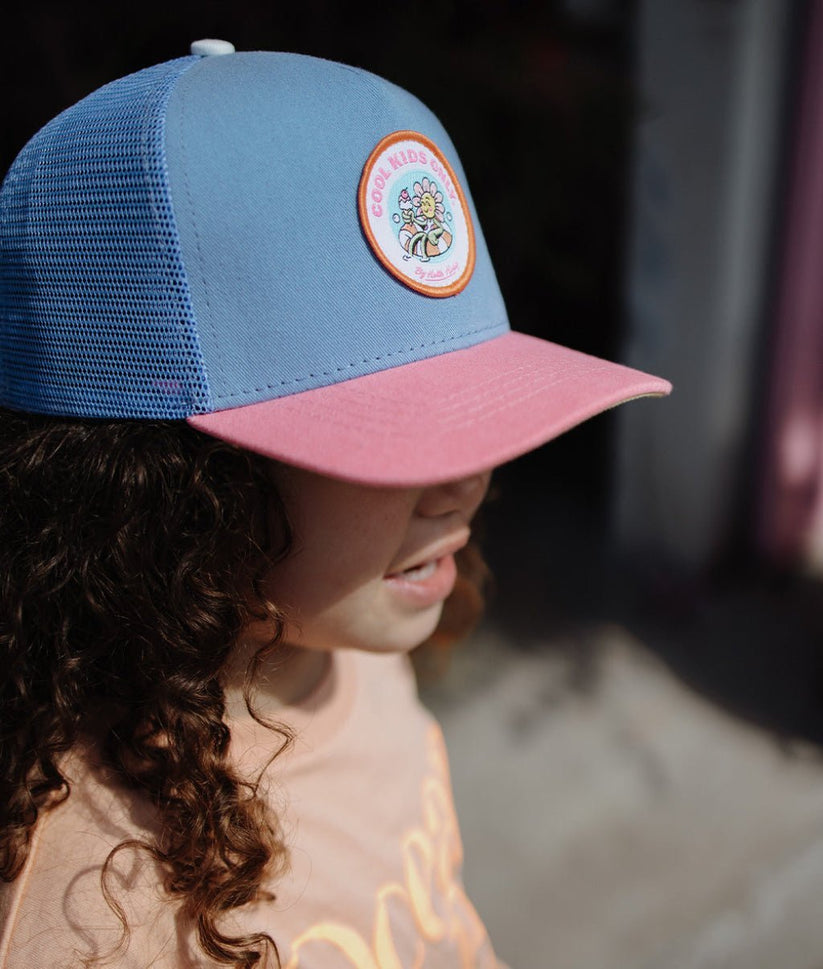 Boné azul e rosa com emblema redondo usado por criança com cabelo encaracolado