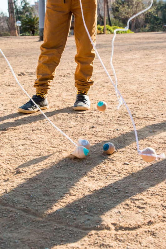 Pessoa jogando piões de madeira com cordas em chão de terra