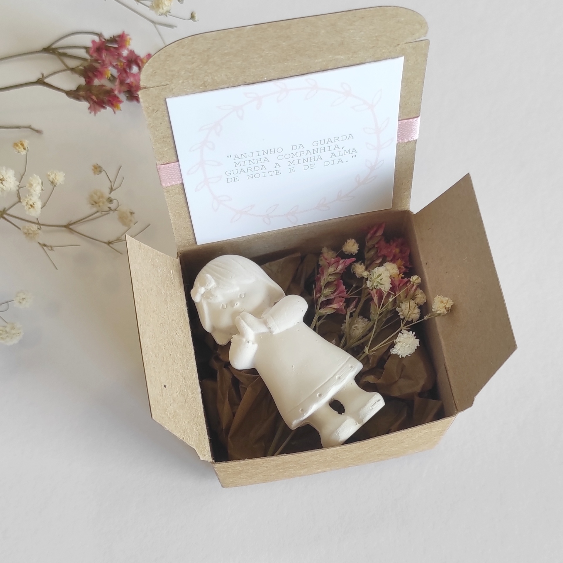 Caixa de papelão com figura de anjo branco, flores secas e cartão com mensagem