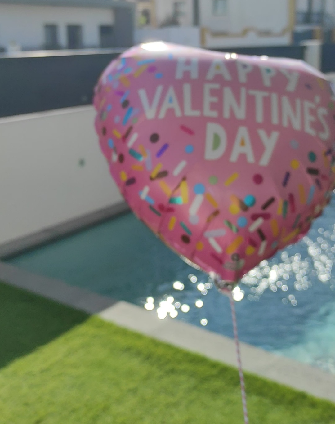 Balão cor-de-rosa em formato de coração com texto Happy Valentine's Day próximo a piscina