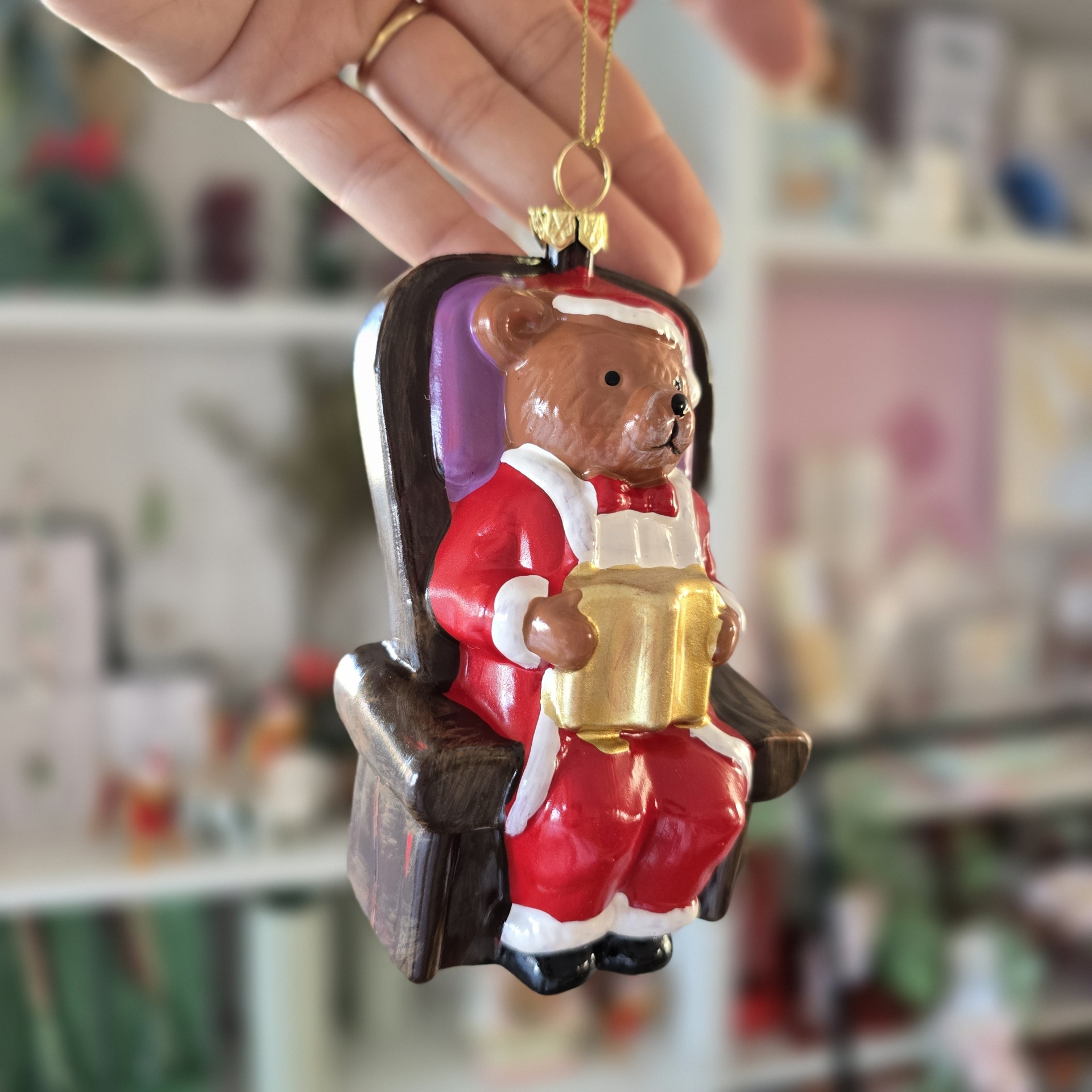 Ornamento de urso vestido de Pai Natal sentado numa cadeira