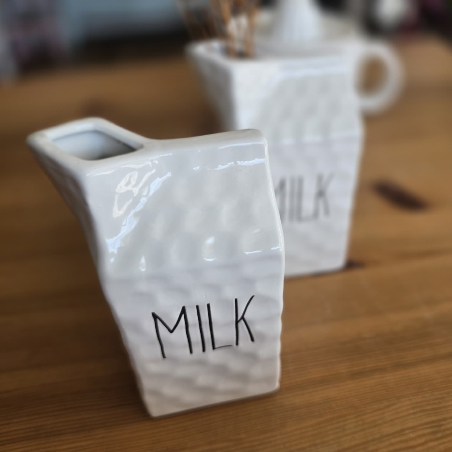 Dois jarros de cerâmica branca com a palavra MILK em mesa de madeira.