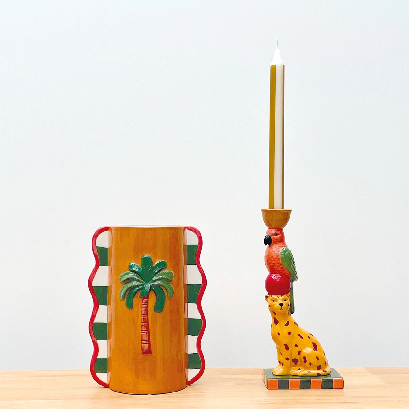 Jarro e castiçal coloridos com decoração de palmeira, leopardo e papagaio e vela acesa