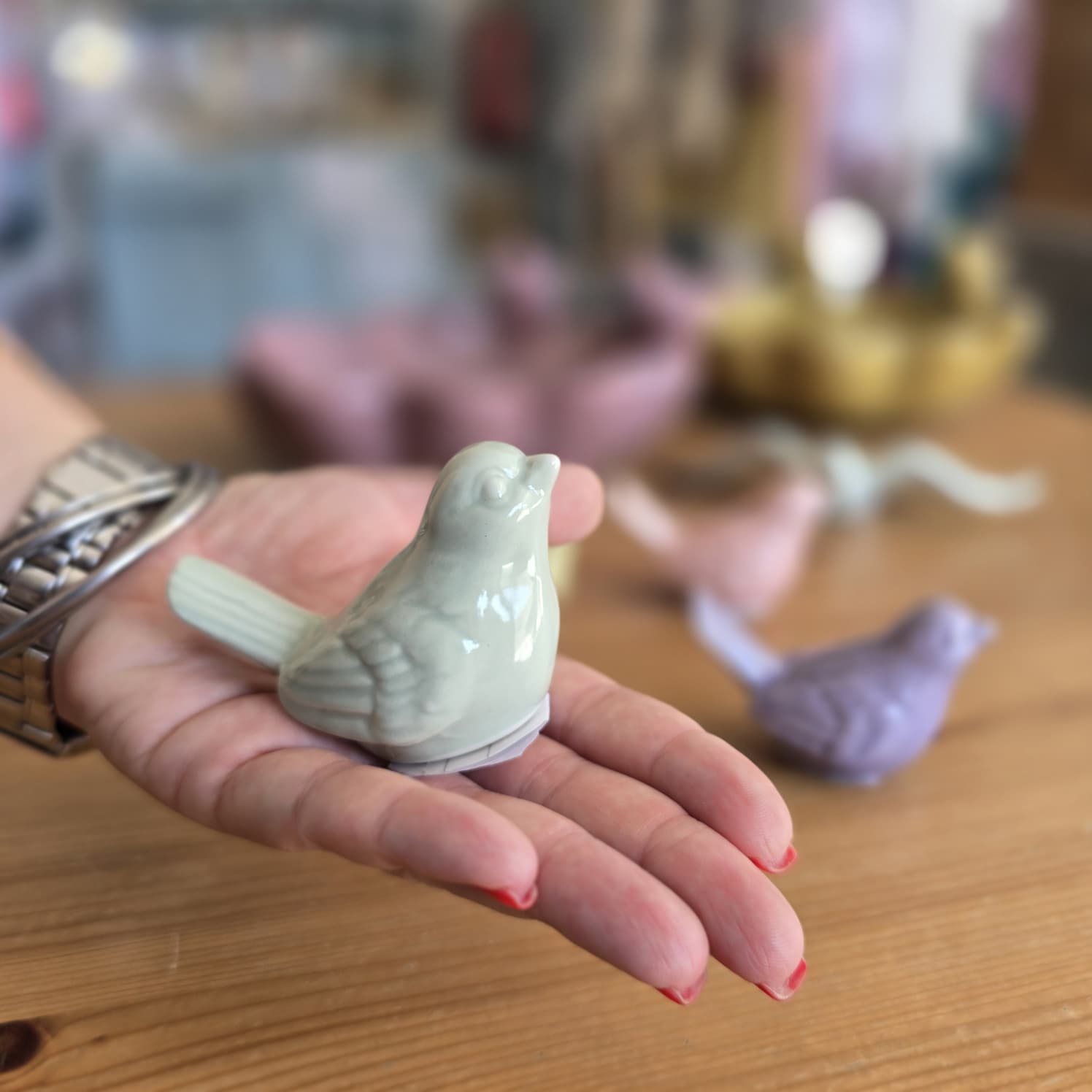 Pássaro de cerâmica cinza na mão sobre mesa com outros pássaros coloridos desfocados