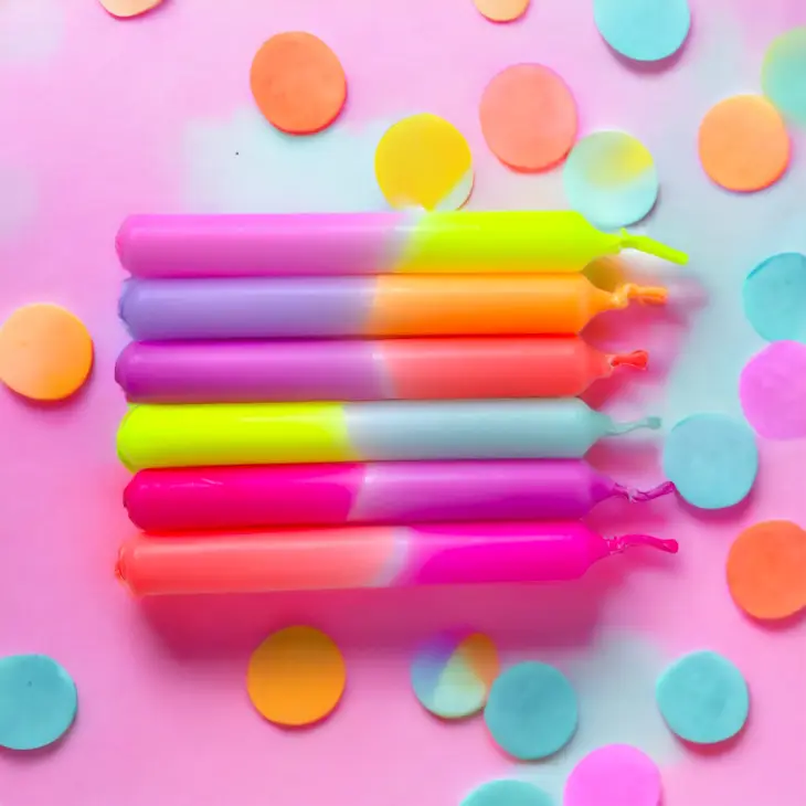 Cinco velas coloridas bicolores para festa com confetes coloridos sobre fundo rosa