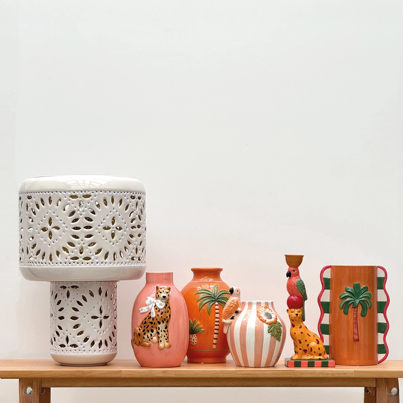 Peças decorativas em cerâmica colorida com motivos de onça, papagaio e palmeira sobre bancada de madeira