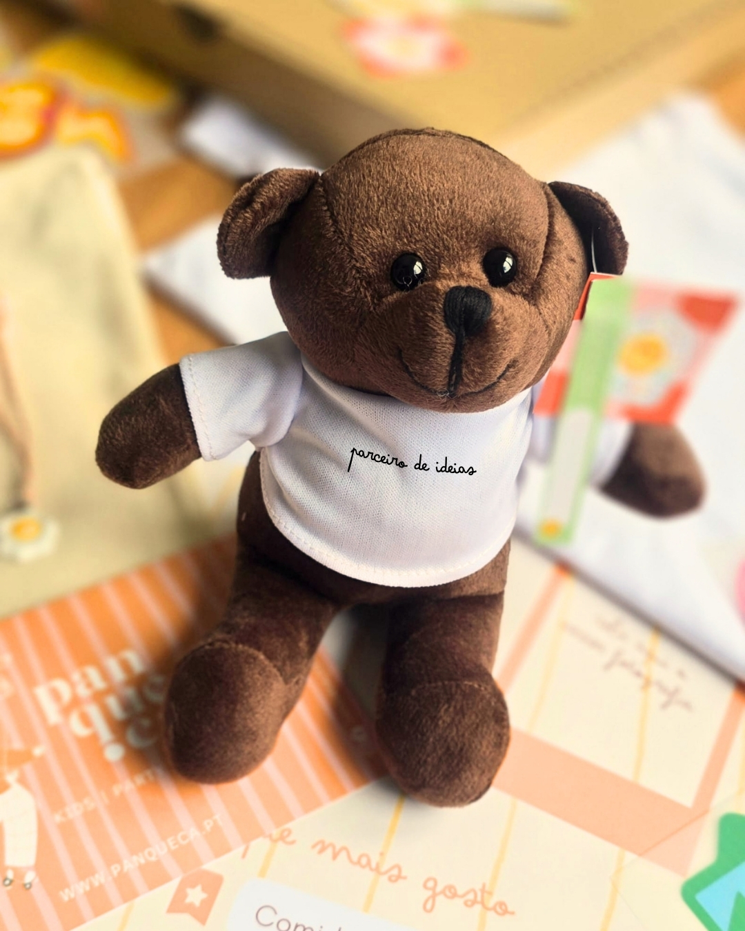 Urso de peluche castanho com t-shirt branca com texto parceiro de ideias