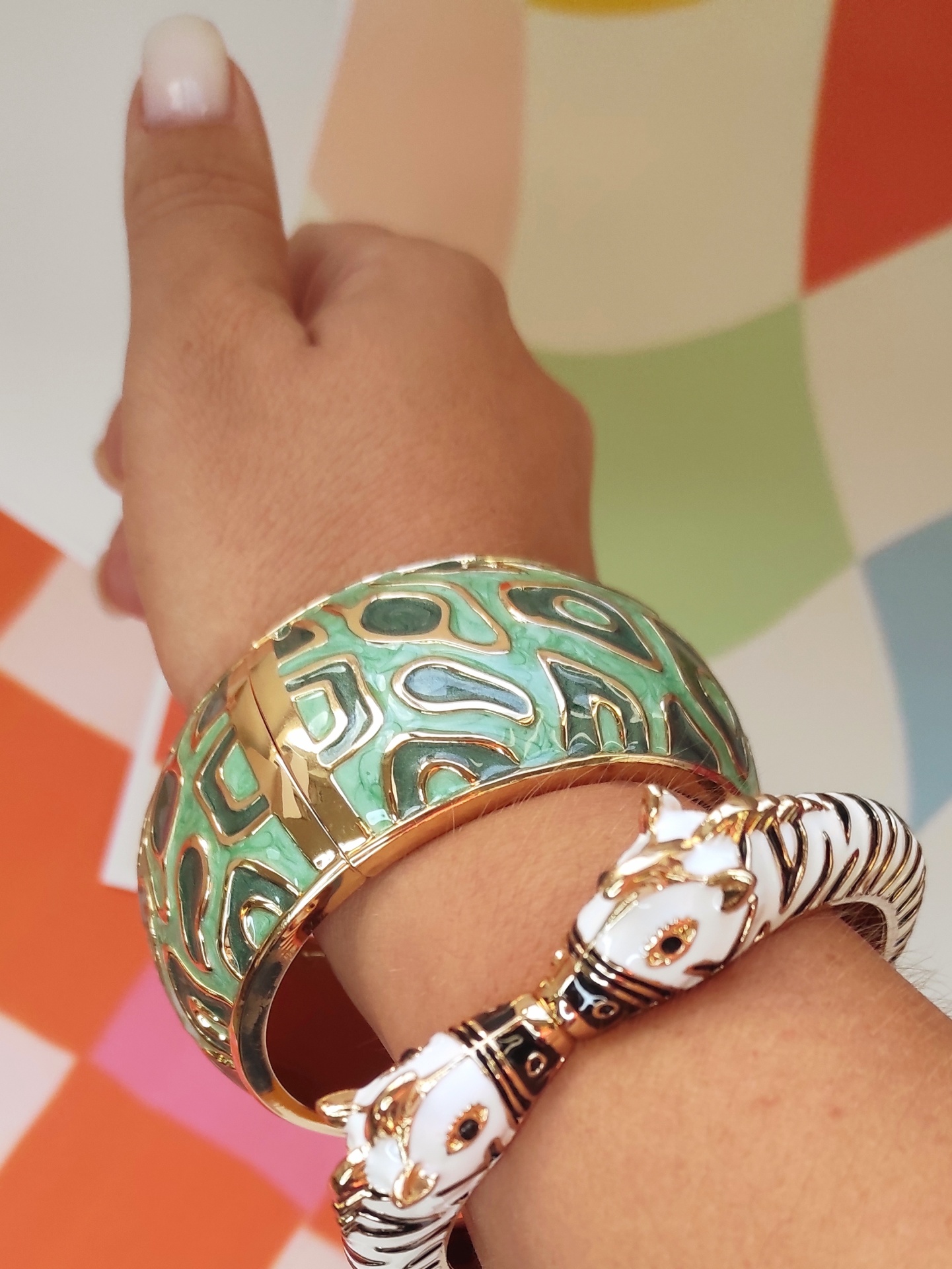 Pulseiras dourada com desenhos verdes e azuis e pulseira em forma de tigre branca e preta num pulso