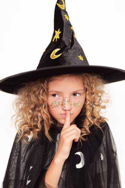 Criança vestida de bruxa com chapéu e capa pretos decorados com luas e estrelas.
