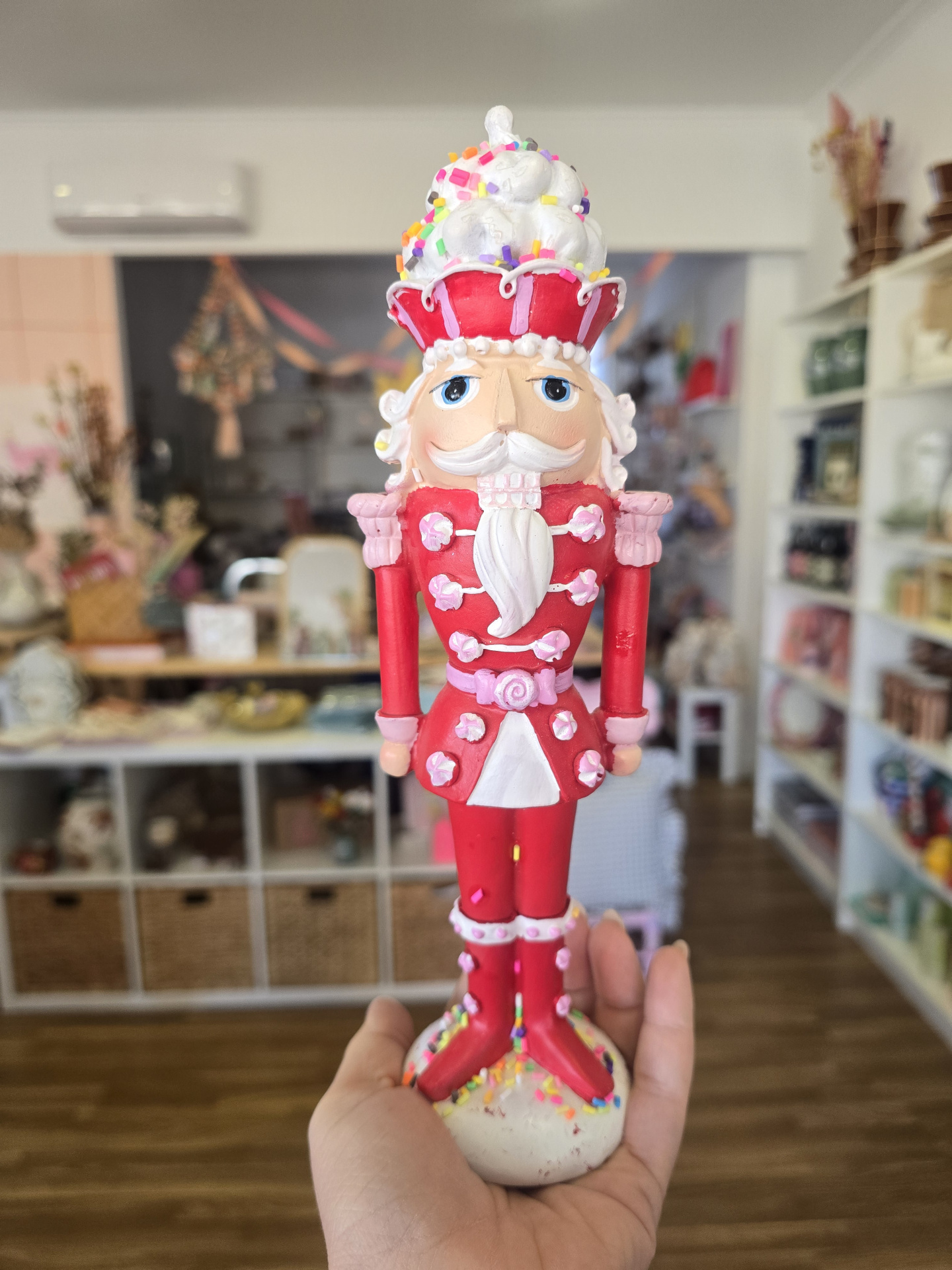Figura Quebra-Nozes em madeira vermelha, branca e rosa com confetis, segurada numa mão em loja.
