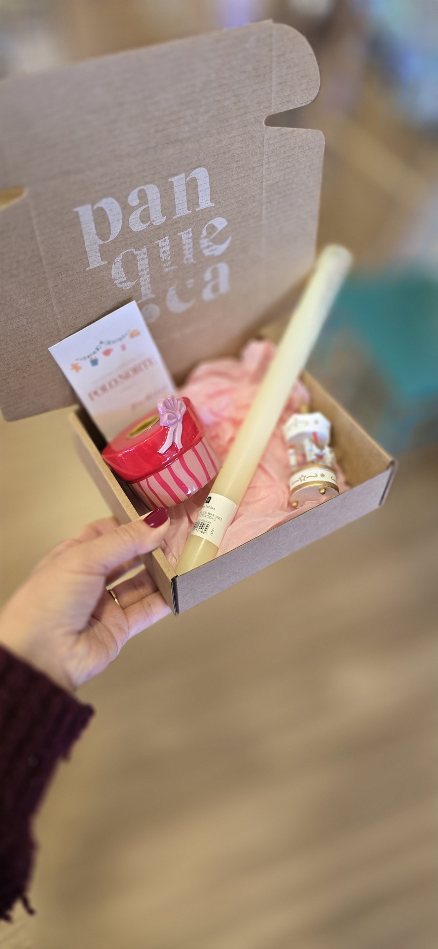 Caixa de cartão com vela, frasco vermelho, papel de seda rosa e mini-rolha branca com etiqueta.