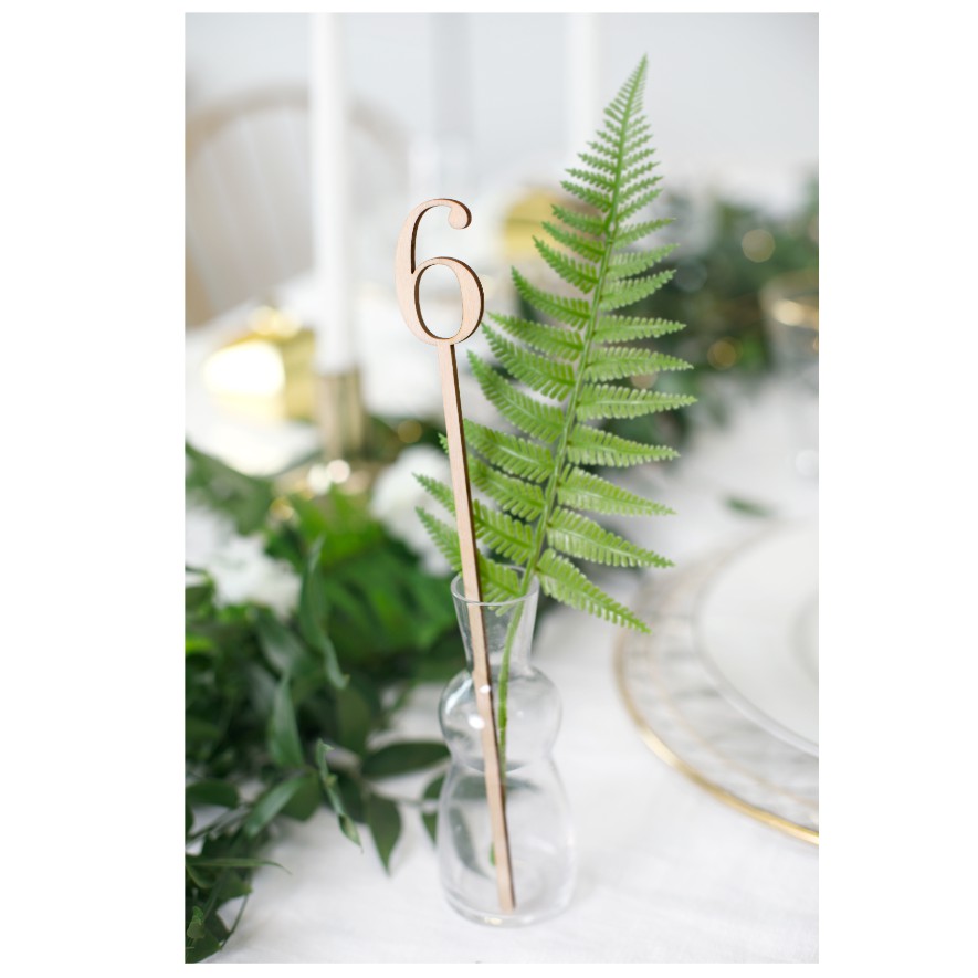 Vaso pequeno de vidro com folha verde e número 6 dourado na mesa decorada