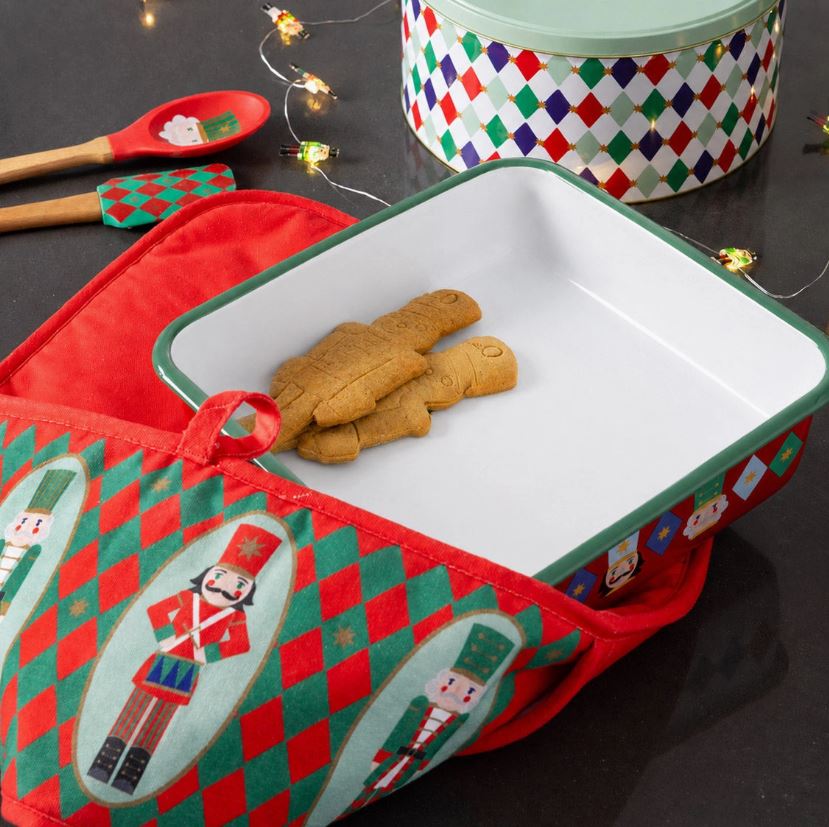 Forma de forno branca e verde com bolachas, luva térmica vermelha e verde e utensílios de cozinha em fundo escuro