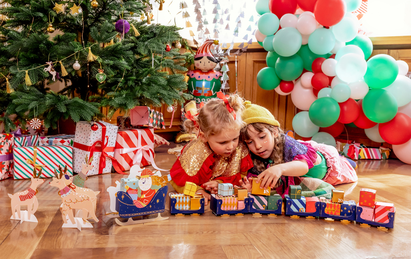 Crianças a brincar com comboio de brinquedo em ambiente decorado para Natal