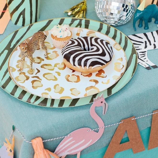 Prato decorativo com padrão animal, cupcake, donut com cobertura zebra e figuras de plástico sobre mesa azul