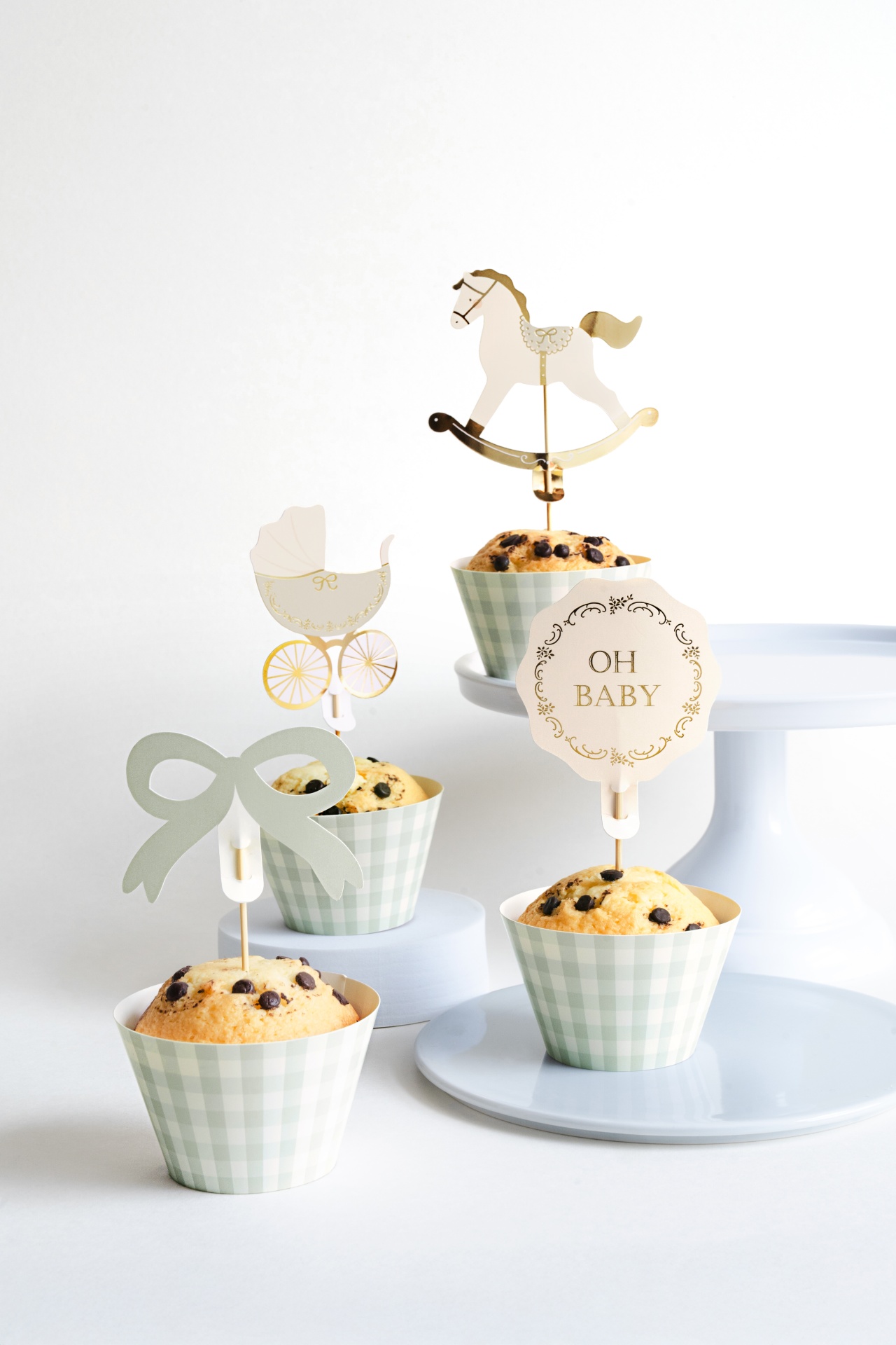 Muffins decorados com toppers de papel para festa de bebé, em formas de padrão xadrez verde sobre suportes brancos.