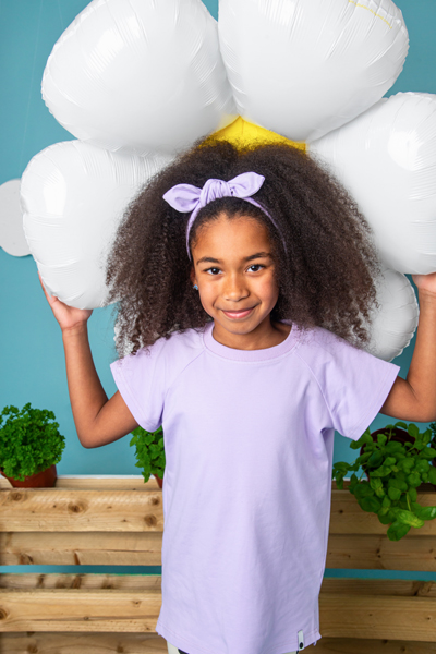 Menina com t-shirt lilás e faixa de cabelo segurando balão em forma de flor
