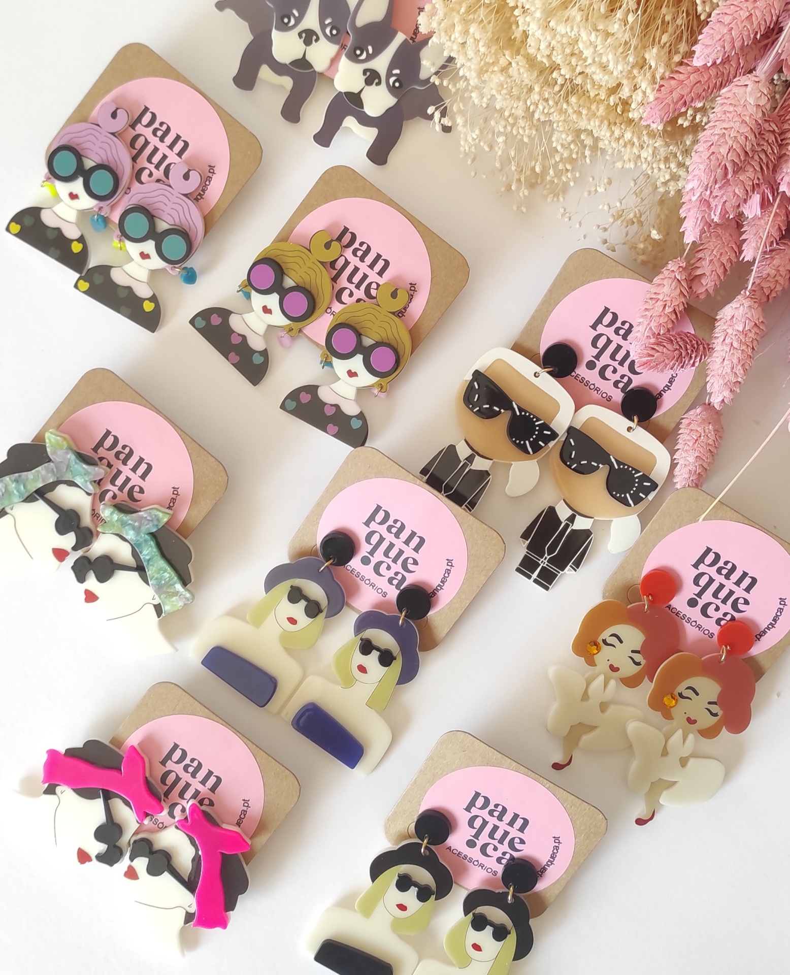 Brincos de acrílico com designs de personagens e cães em cartões rosa com texto 'pan que ce'