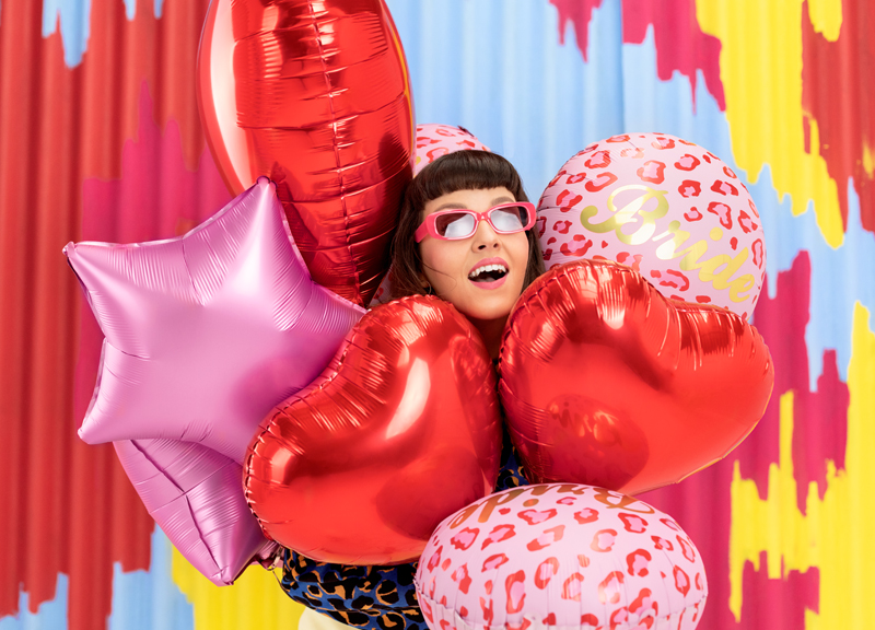 Mulher com balões metálicos vermelhos e rosa e fundo colorido abstrato