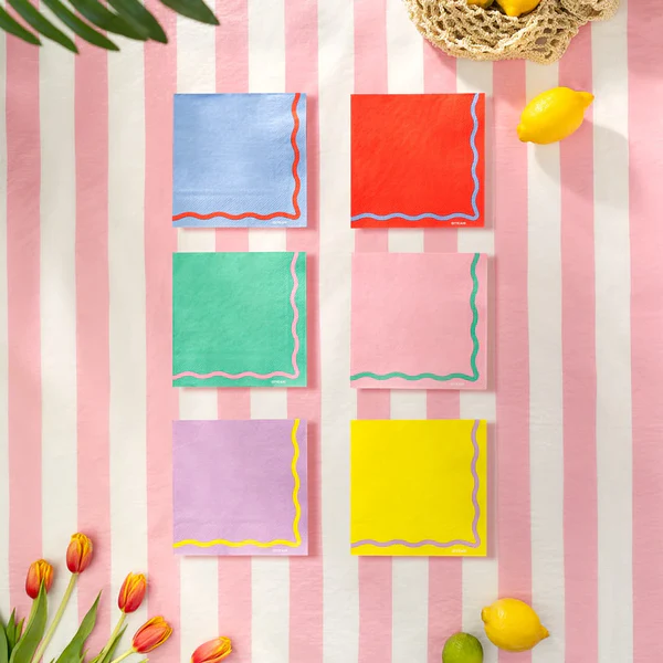 Seis guardanapos coloridos com bordas onduladas em toalha riscada rosa e branca com frutas e flores