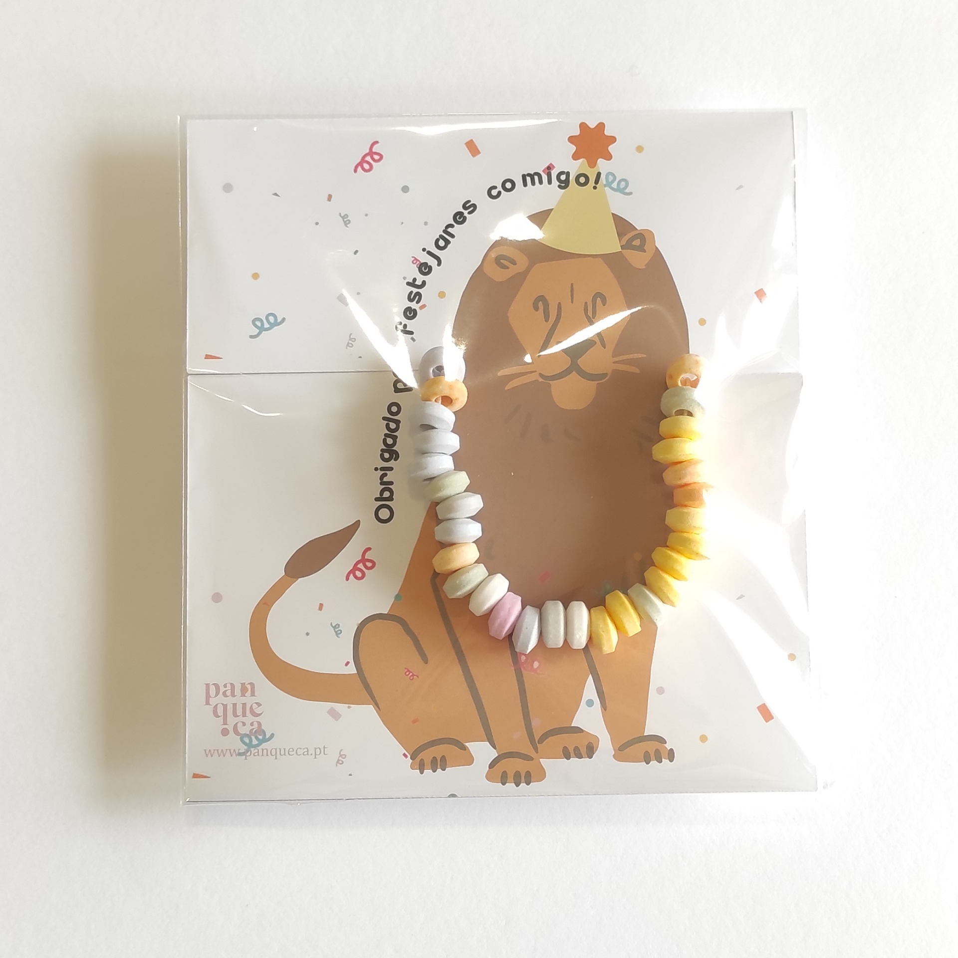 Pulseira colorida com contas pequenas sobre cartão ilustrado com leão e texto de agradecimento