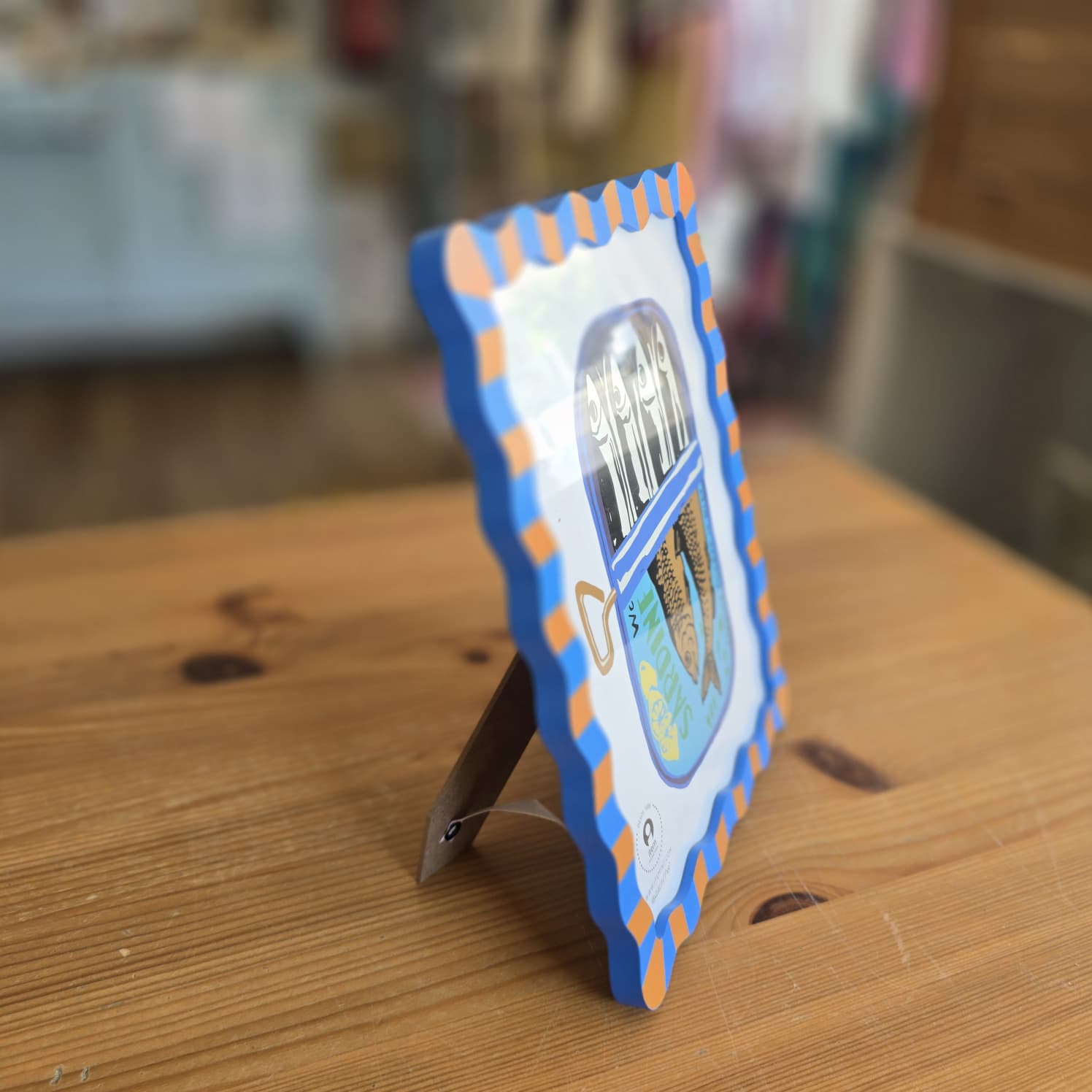 Placa decorativa em madeira com moldura ondulada azul e laranja sobre mesa de madeira