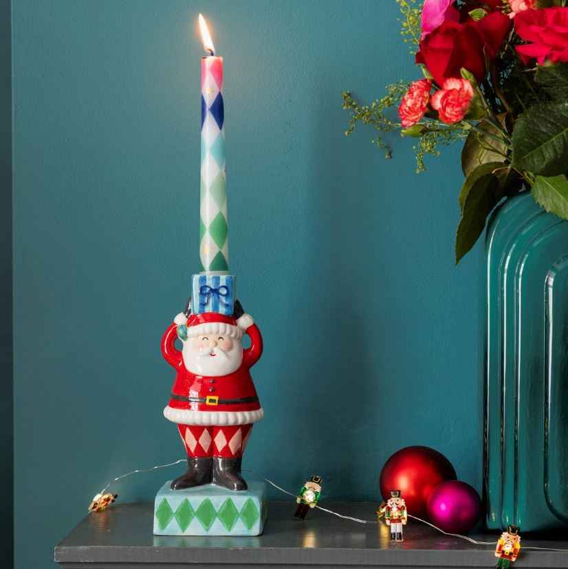 Castical com figura de Pai Natal a suportar vela colorida em tampo junto a vaso azul e bolas de Natal
