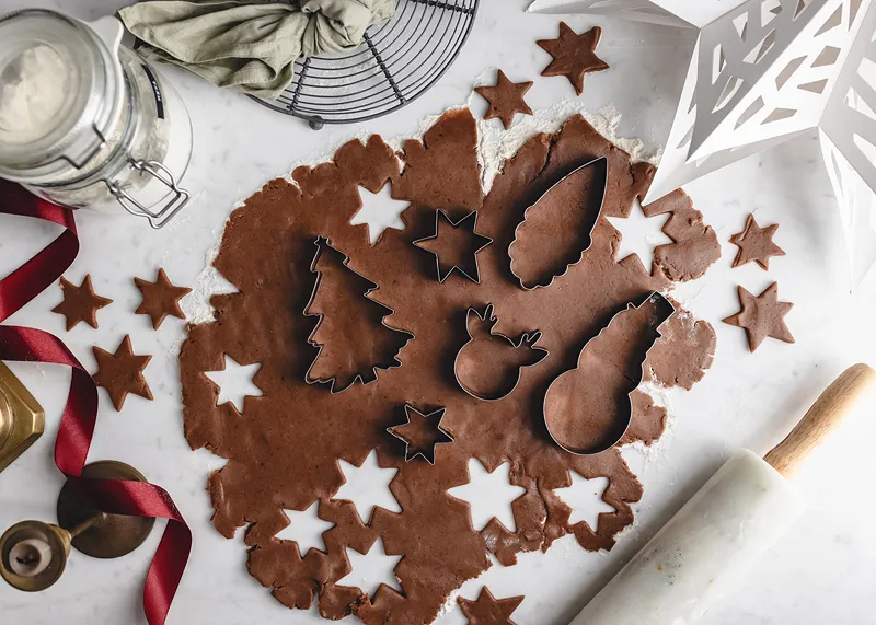 Massa de biscoito castanha com cortadores metálicos em vários formatos sobre superfície branca.
