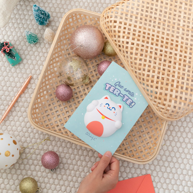 Caixa de vime com cartão azul e gato da sorte rodeada por bolas decorativas brilhantes