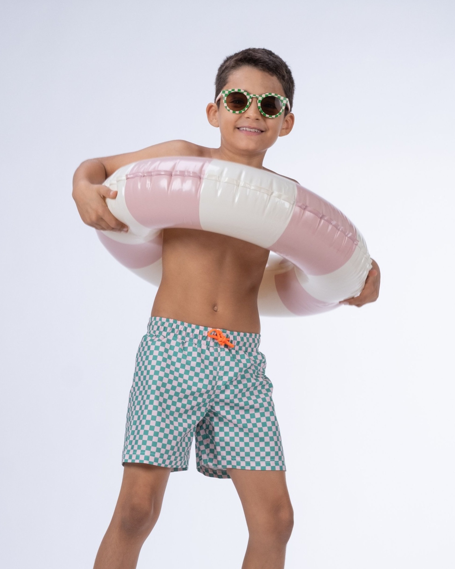 Menino com bóia insuflável branca e rosa e calções de banho quadriculados azul e branco