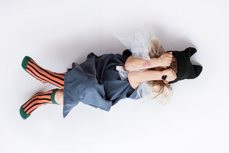 Criança de vestido azul, meias laranja e pretas e chapéu preto deitada