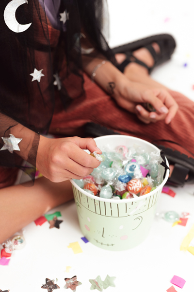 Baldes com doces coloridos embrulhados, confetes coloridos, pessoa vestindo roupa preta e vermelha