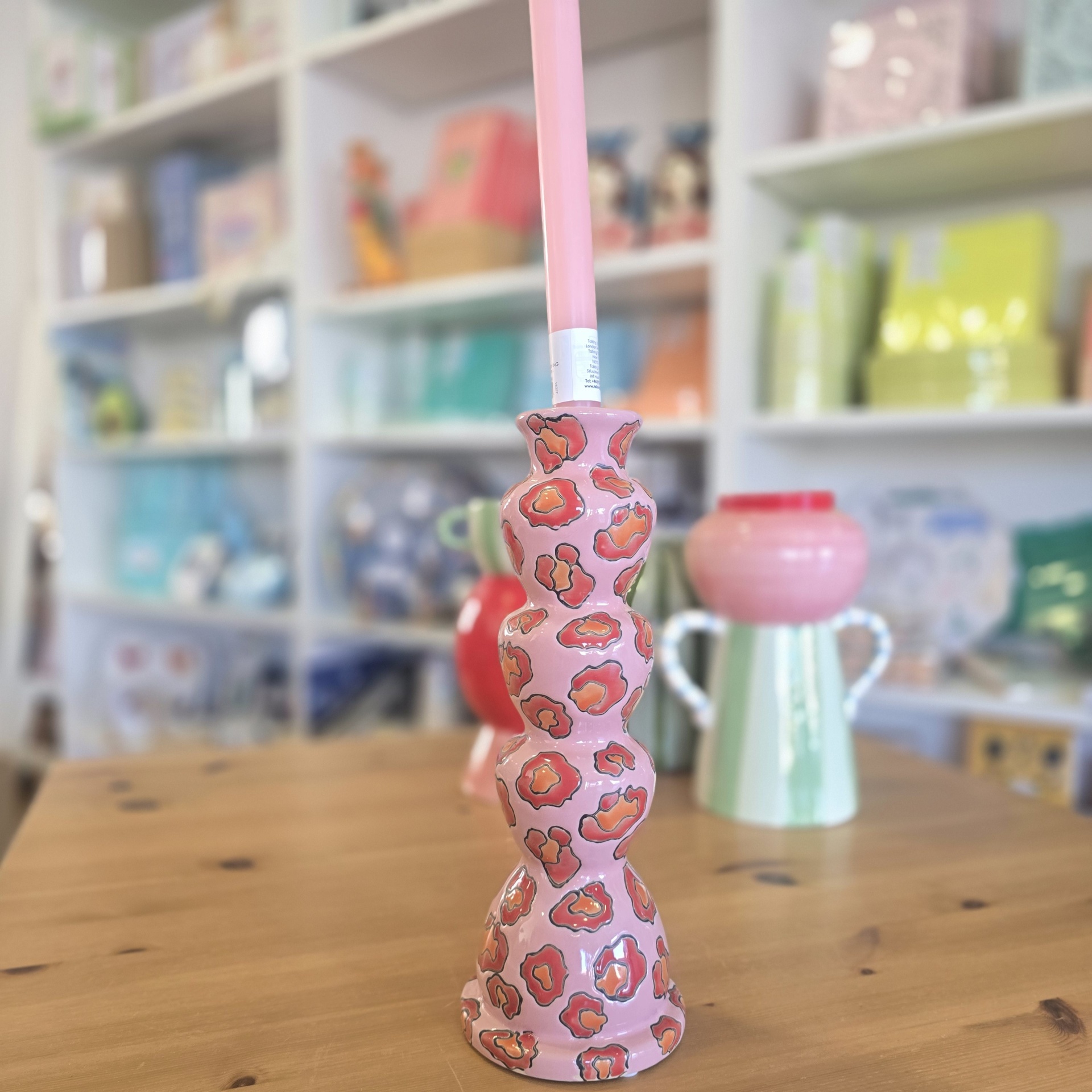 Castical cor de rosa com padrão manchado laranja e preto com vela cor de rosa numa mesa de madeira