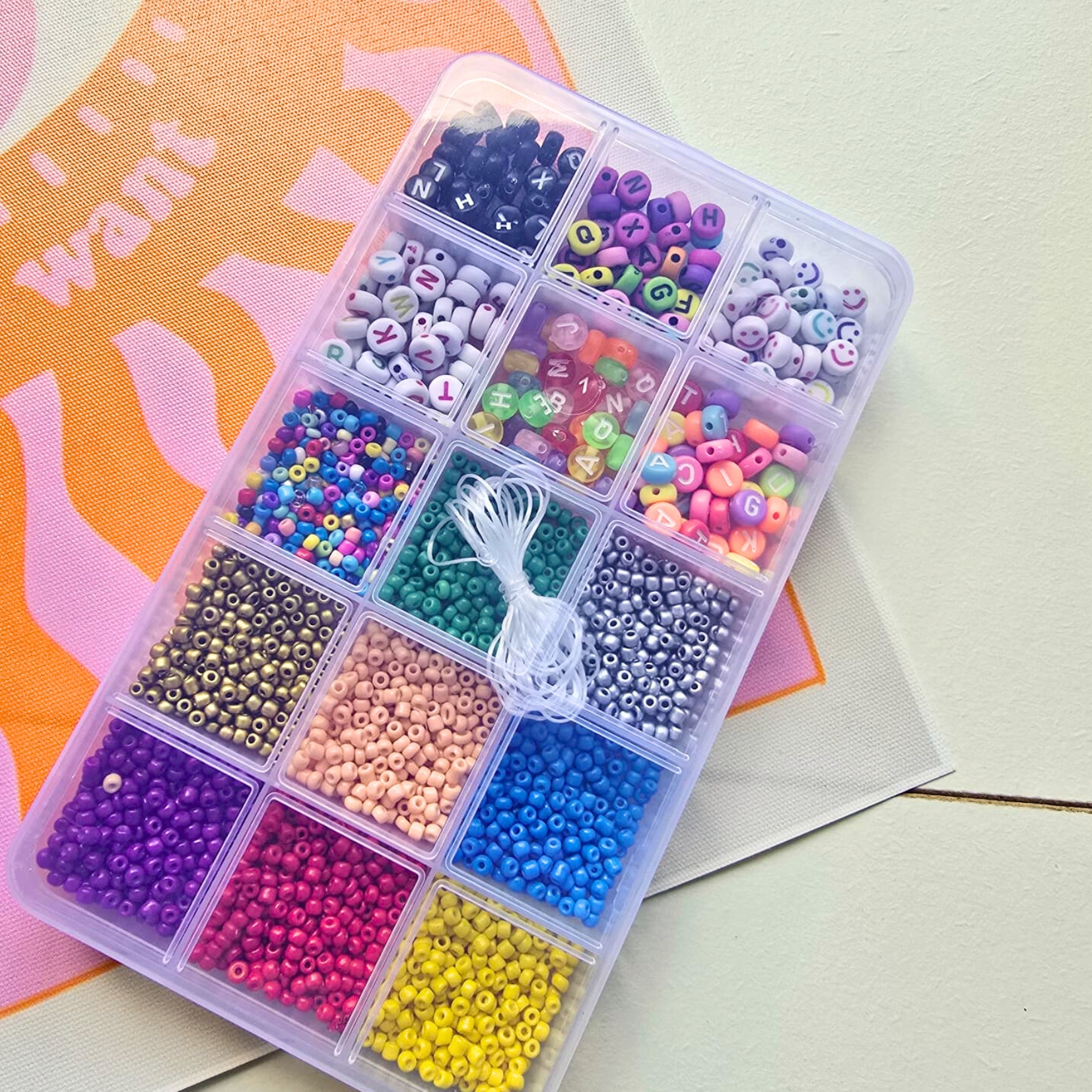 Caixa de plástico com missangas coloridas e fio branco para bijuterias.