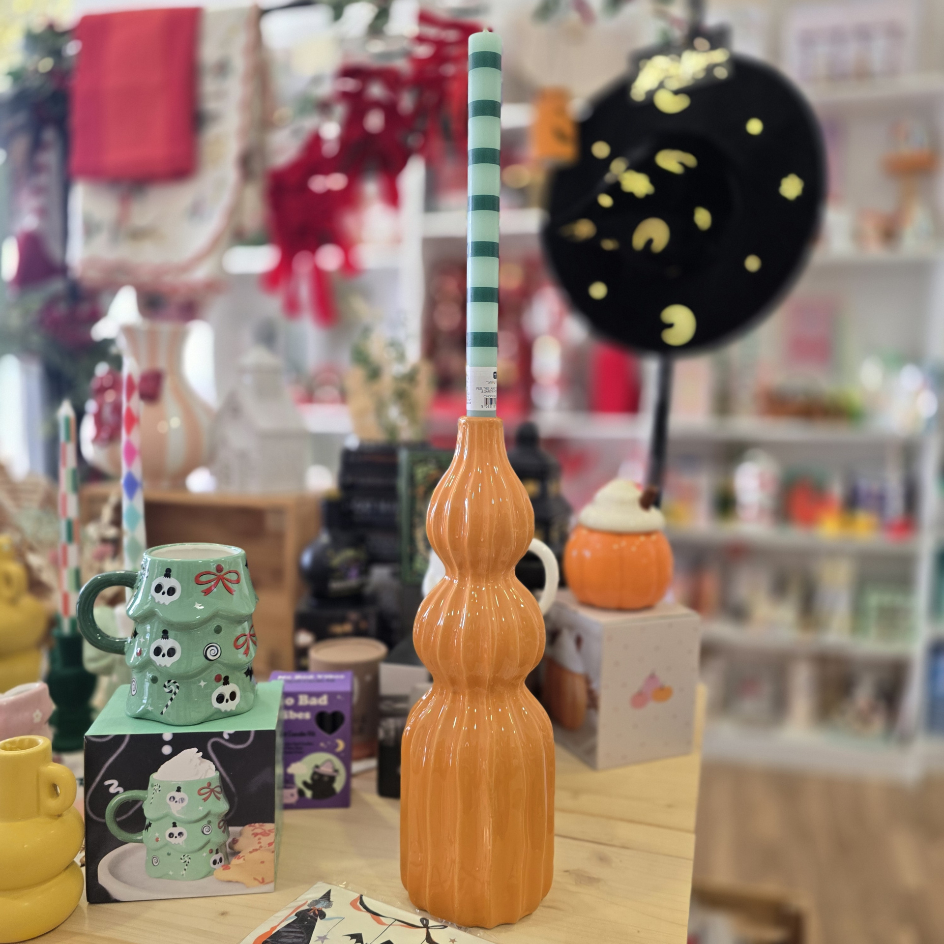Vela verde e branca com suporte laranja em mesa com canecas e decoração