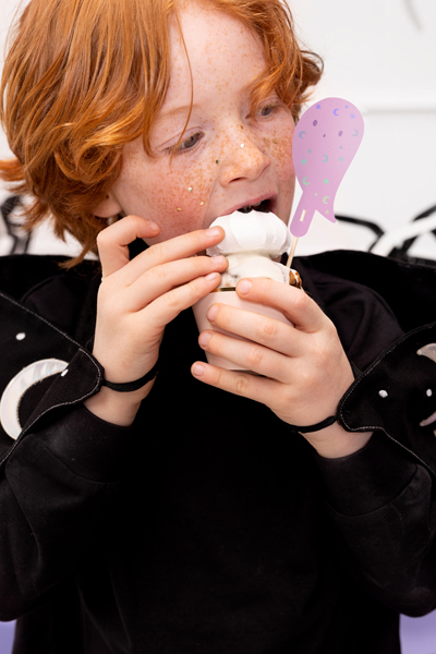 Pessoa a comer gelado com cone e cobertura branca, com camisola preta e cabelo ruivo